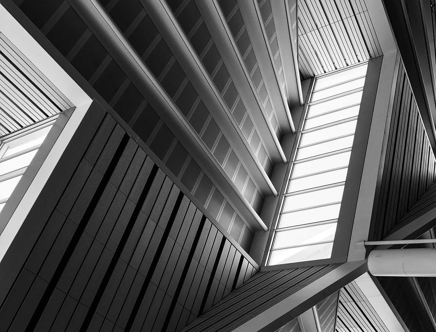 Black and white upward view of angular architectural beams and a skylight, geometric pattern, moody monochrome atmosphere